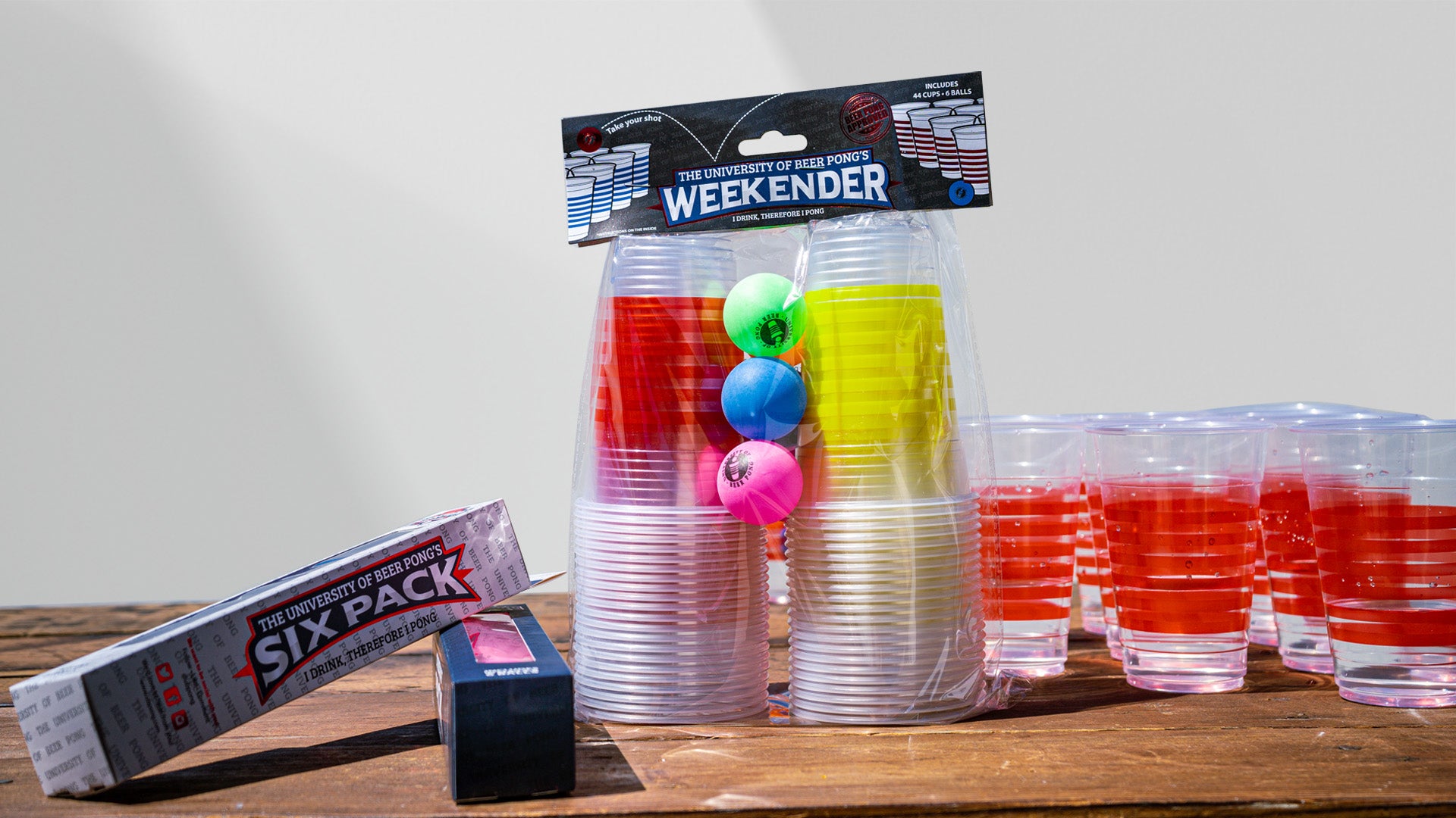 The University of Beer Pong Weekender pack inside its packaging. Displayed on a table beside a group of plastic cups with water.